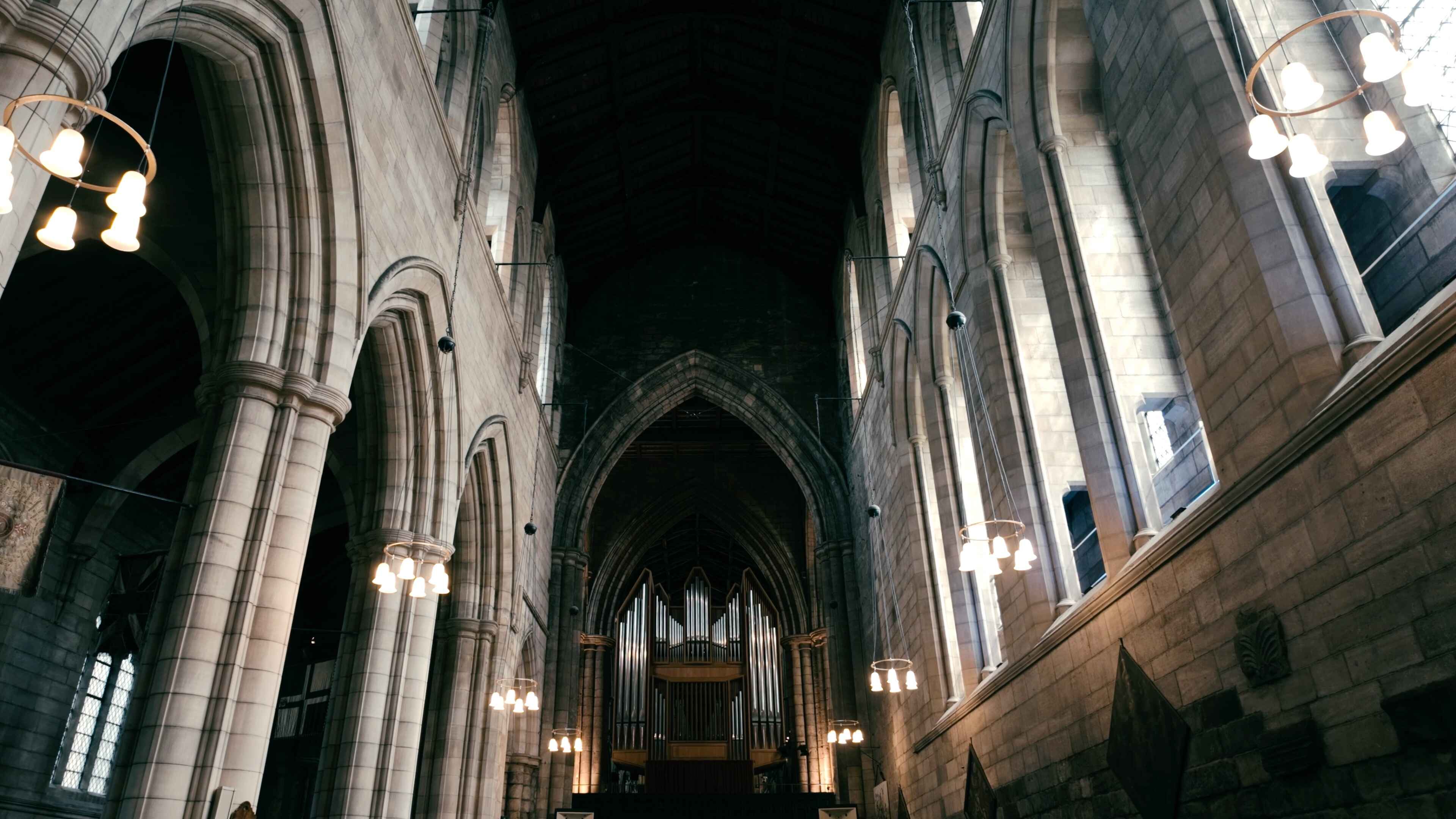 A large, intricately designed organ in the centre of an abbey with archways and windows either side