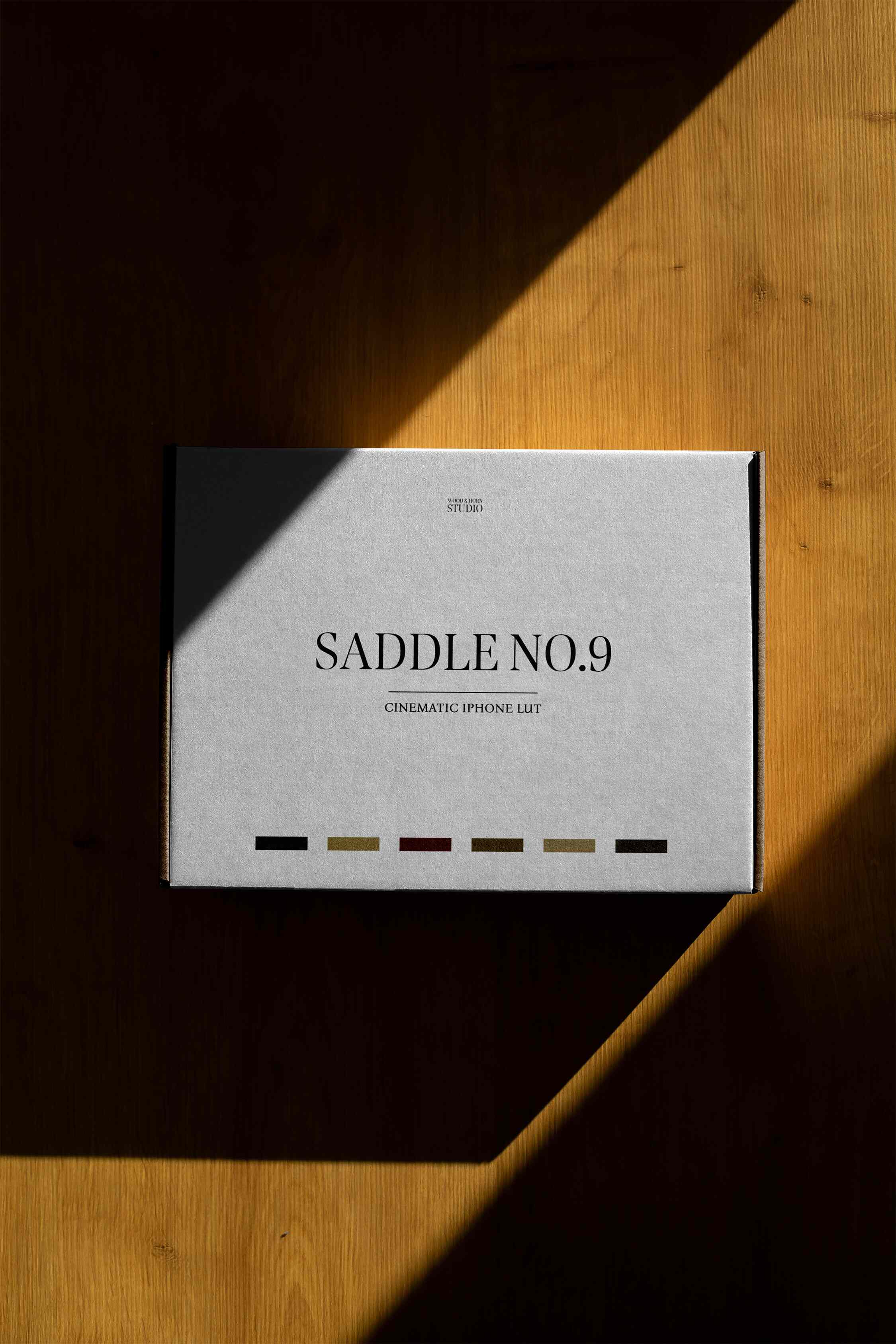 A packaging mockup with the title "SADDLE NO.9" imprinted on the front resting on a wooden surface