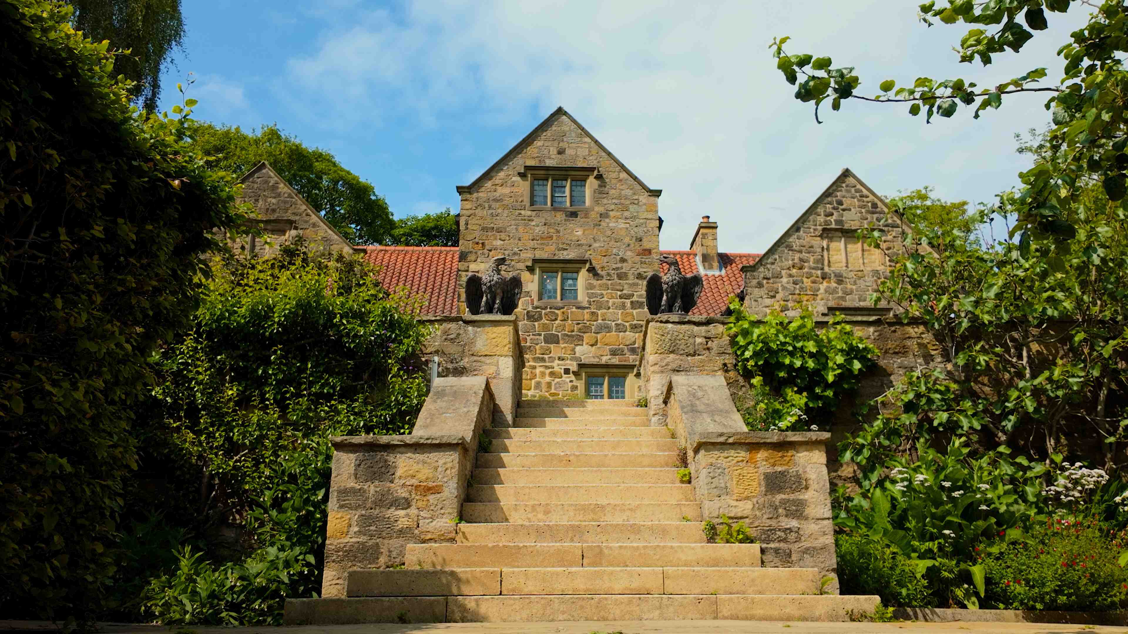 A majestic 17th Century home with steps leading up and two stone birds ordaining both sides under a blue sky