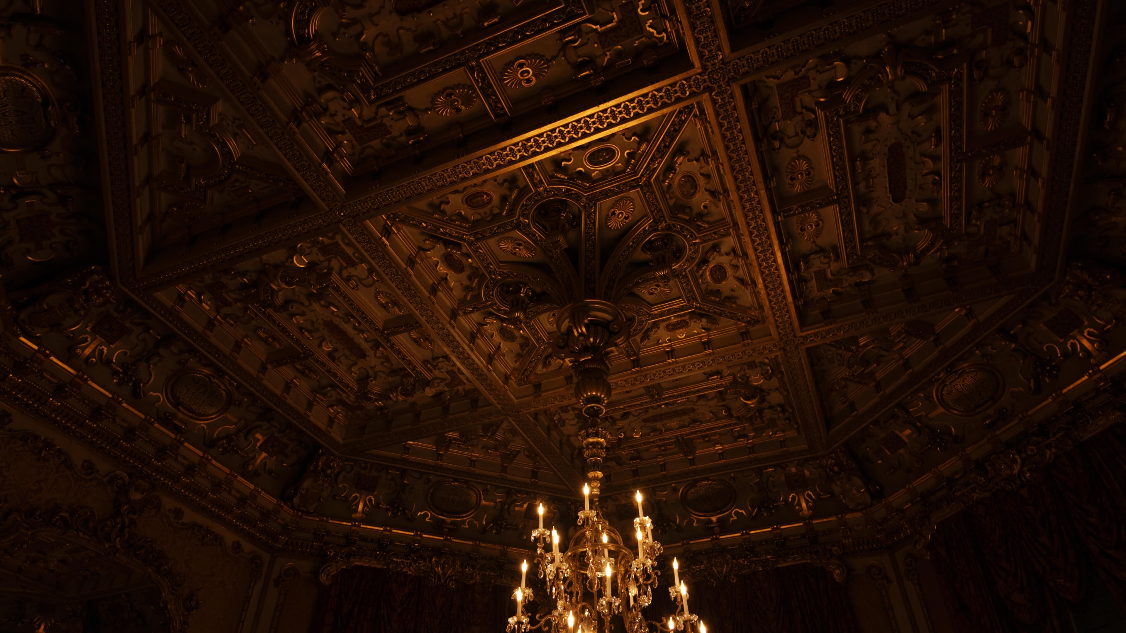  A chandelier glows brightly in a room featuring an intricately designed ceiling