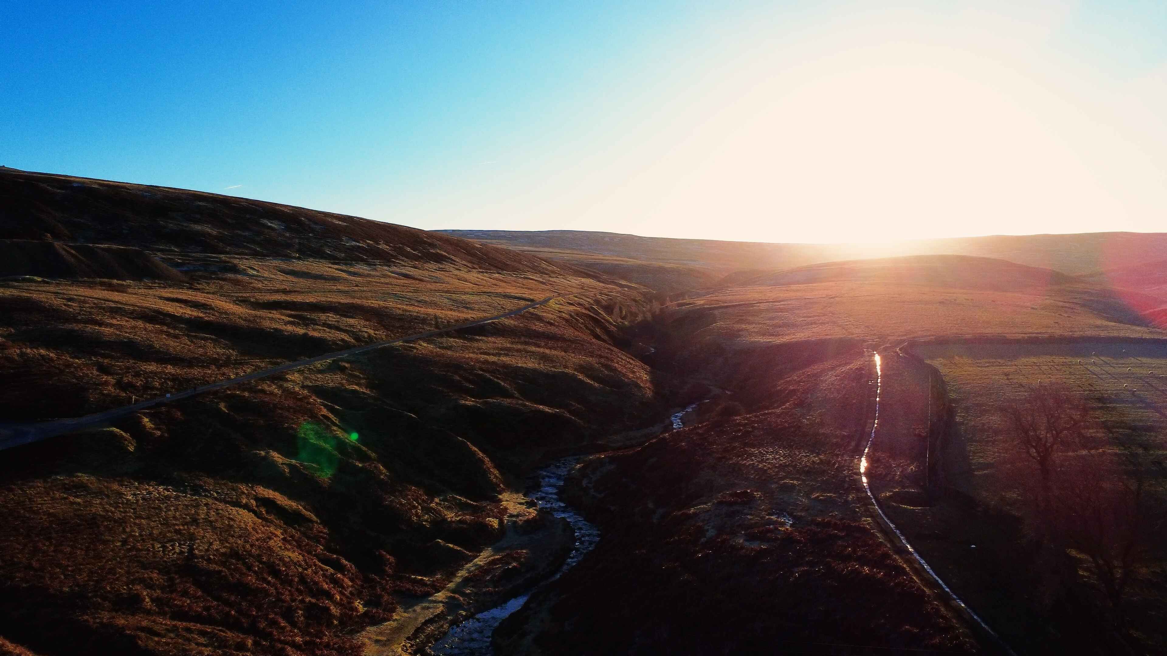 A thin rivulet running through golden hills with a low sun in the back right