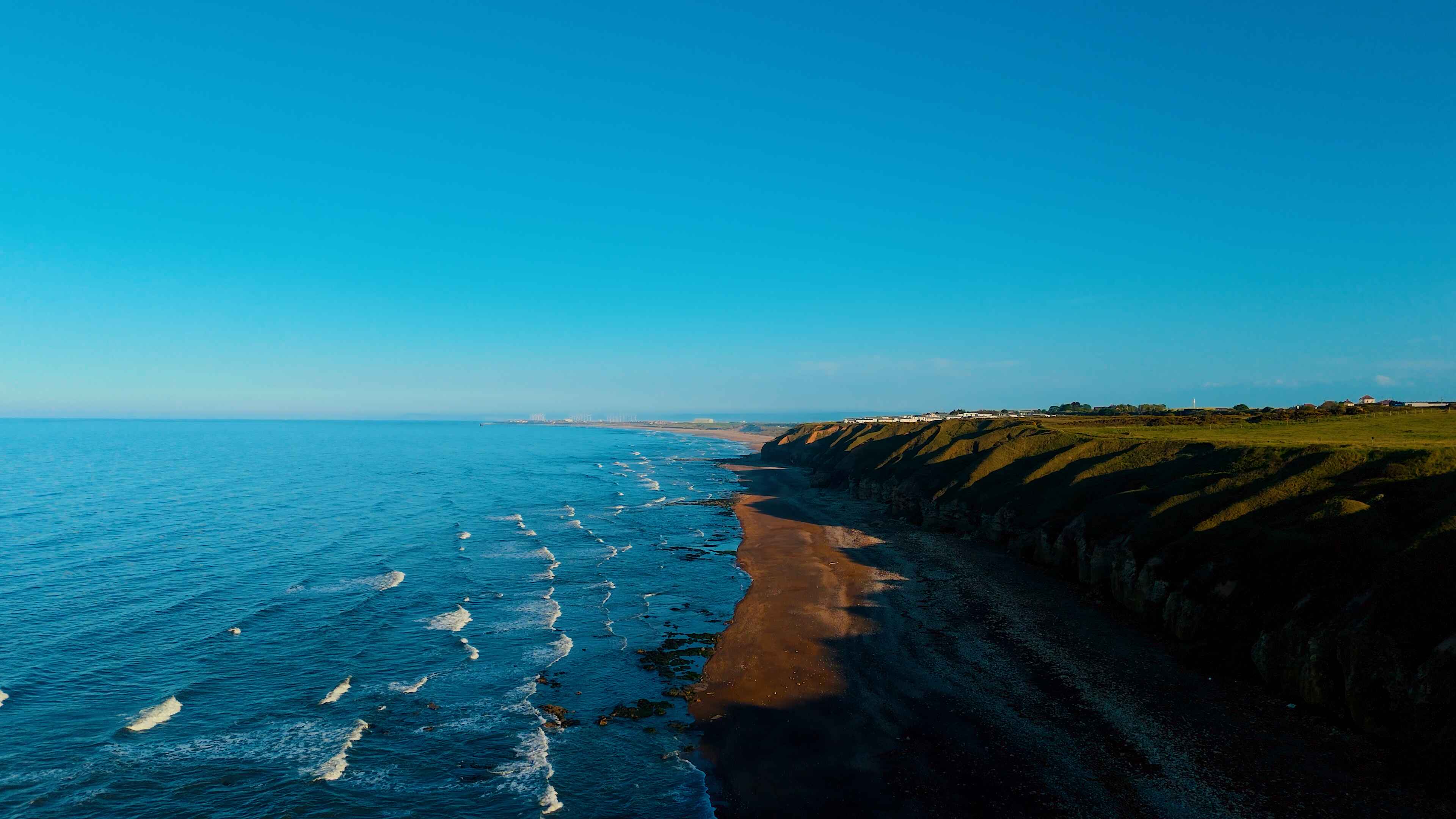 Striking blue water to the left laps over dark-shaded sands under a blue sky