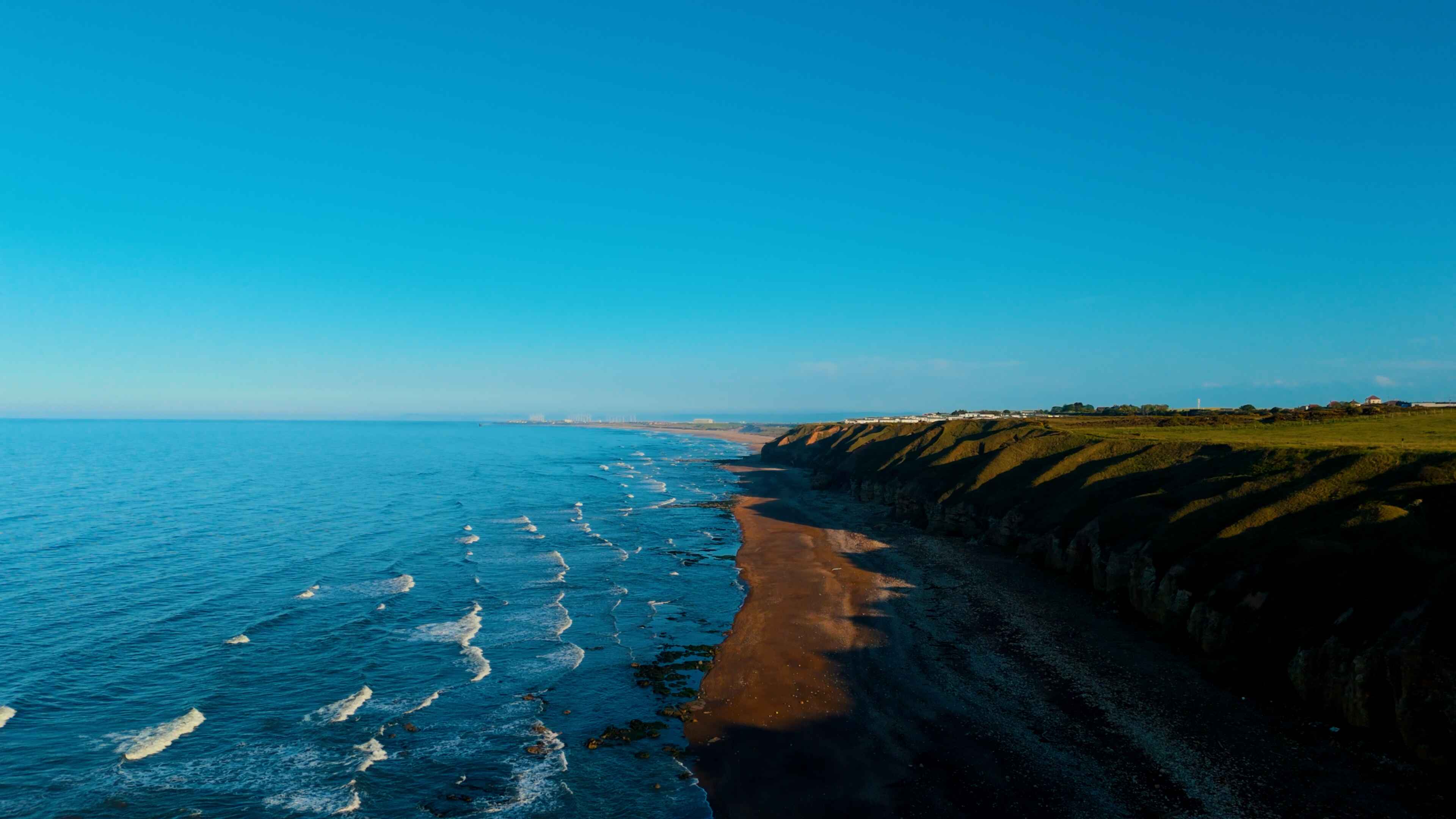 A bright blue ocean meeting black sands at the foothills of steep cliffs