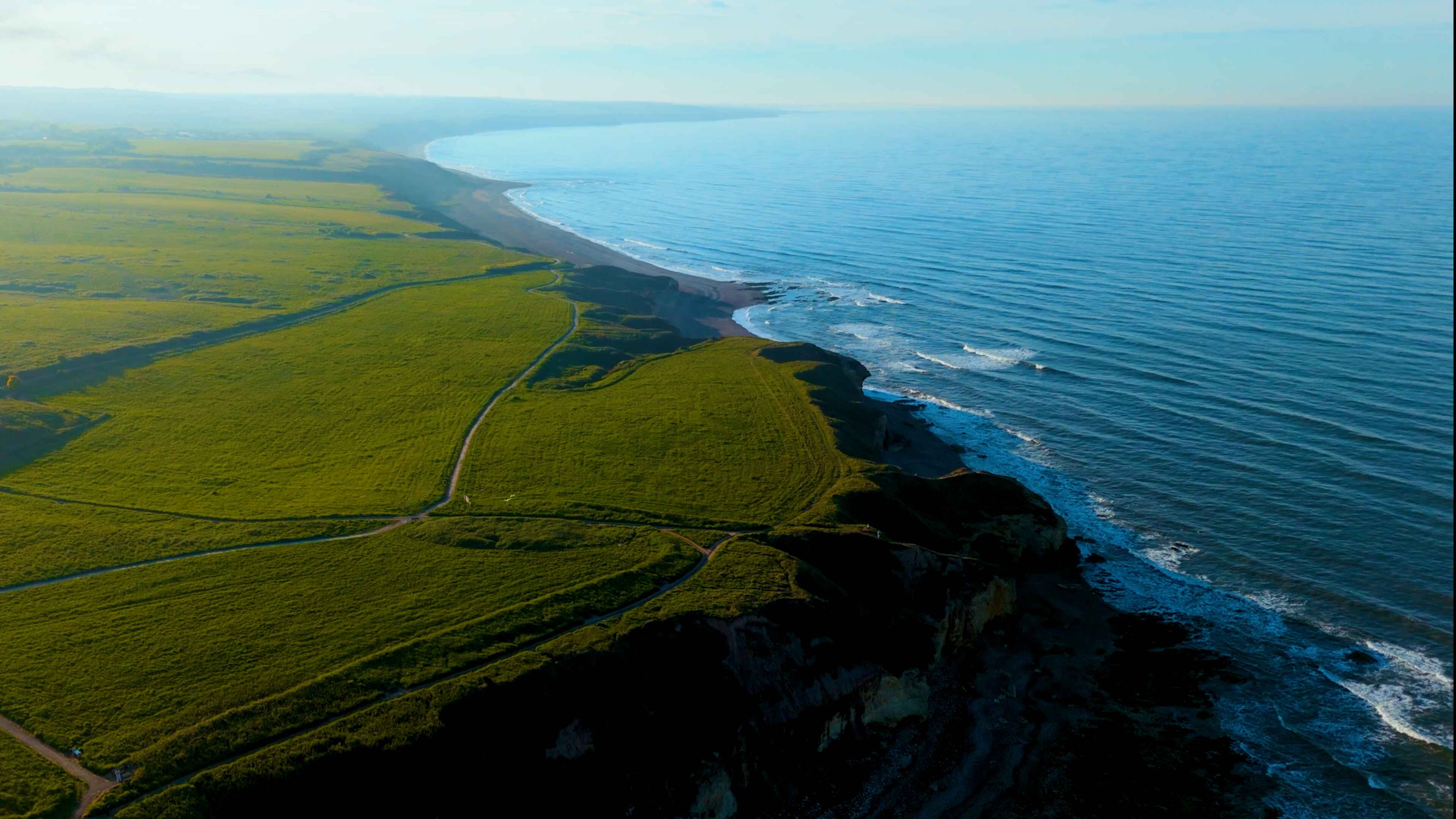 Lush green cliffs to the left overlook a large body of beach-front water