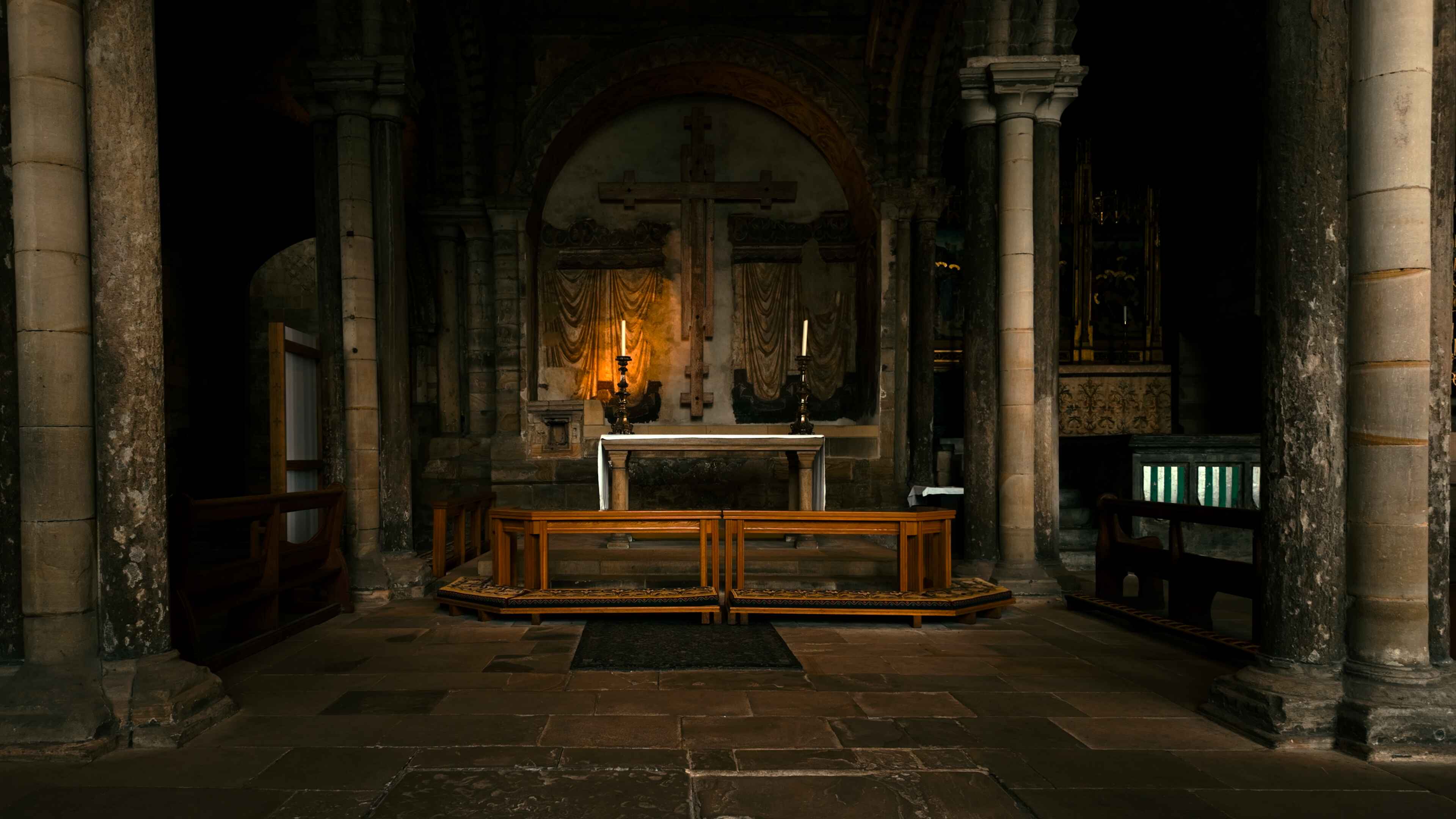 Interior view of a church featuring a wooden bench and two candles either side, with soft lighting illuminating the serene atmosphere.