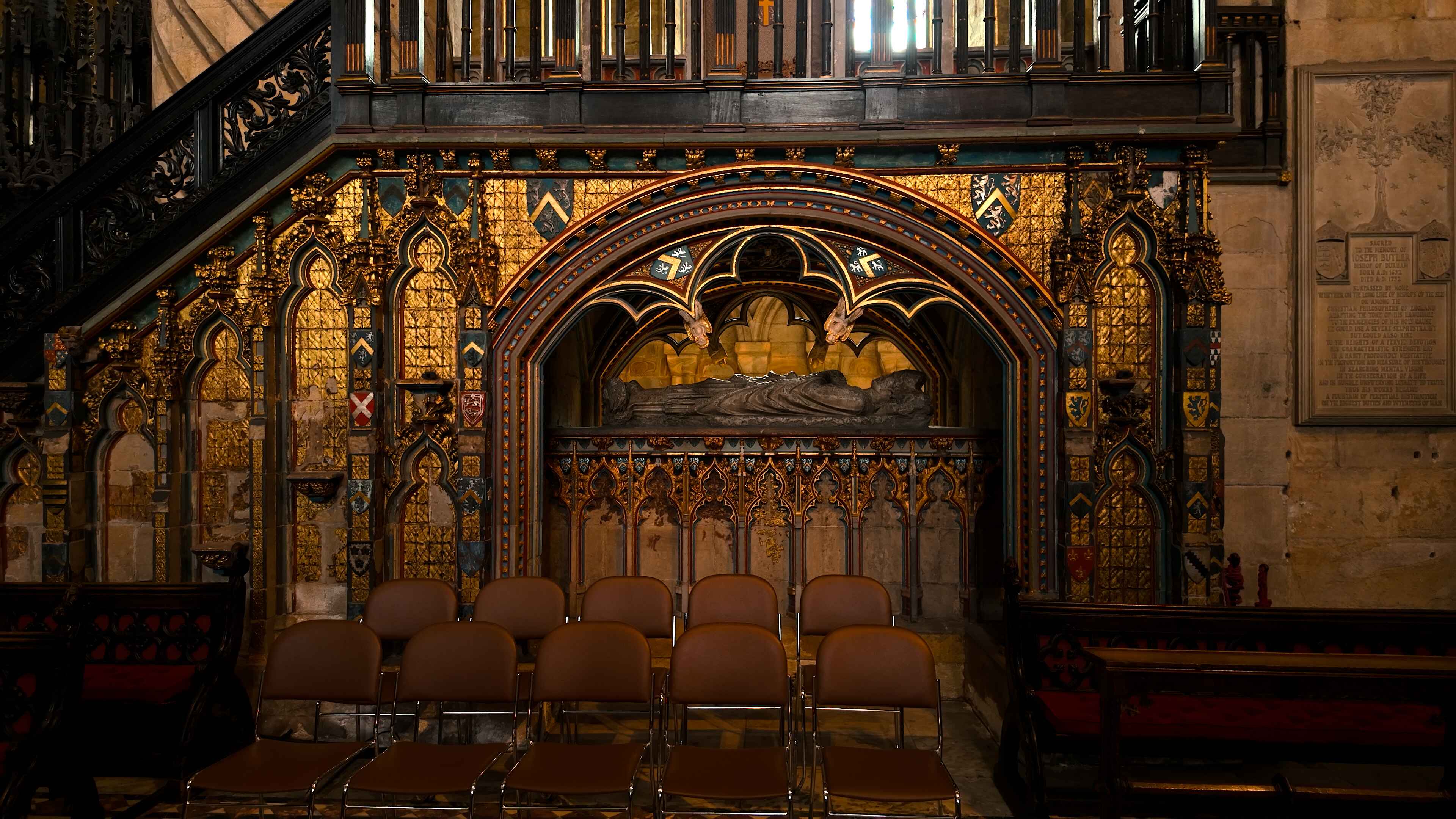 A crypt underneath an intricately designed golden platform with chairs in the foreground